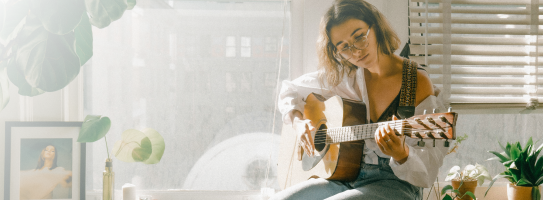Evinde akustik gitar çalan bir müzisyen